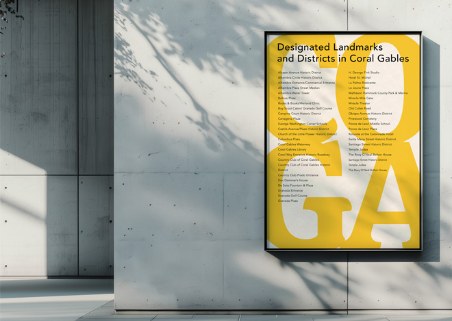 Framed yellow poster on a light concrete wall about designated landmarks and districts in Coral Gables (title reads 'Designated Landmarks and Districts in Coral Gables').