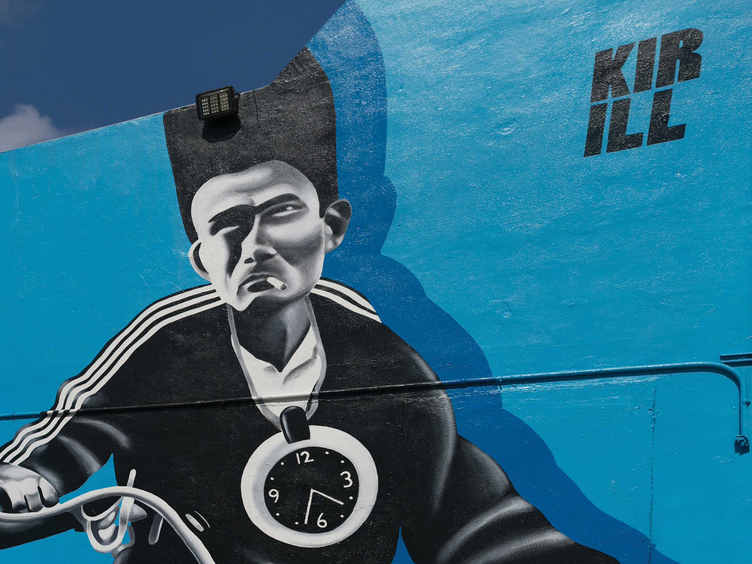 Blue wall mural of a monochrome man in a suit with a large clock on his chest, set against a bright blue background.