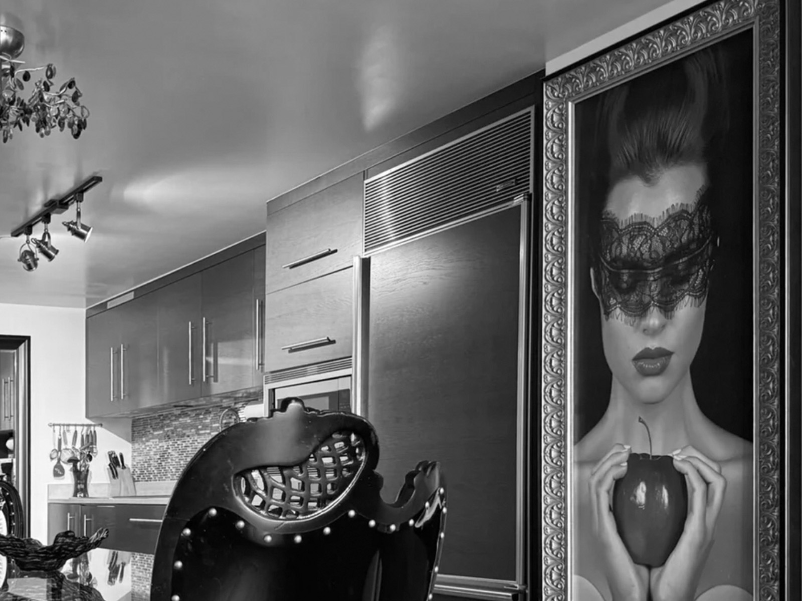 Contemporary kitchen showroom with glossy gray cabinets and an ornate framed black‑and‑white portrait of a lace‑masked woman at the right edge.