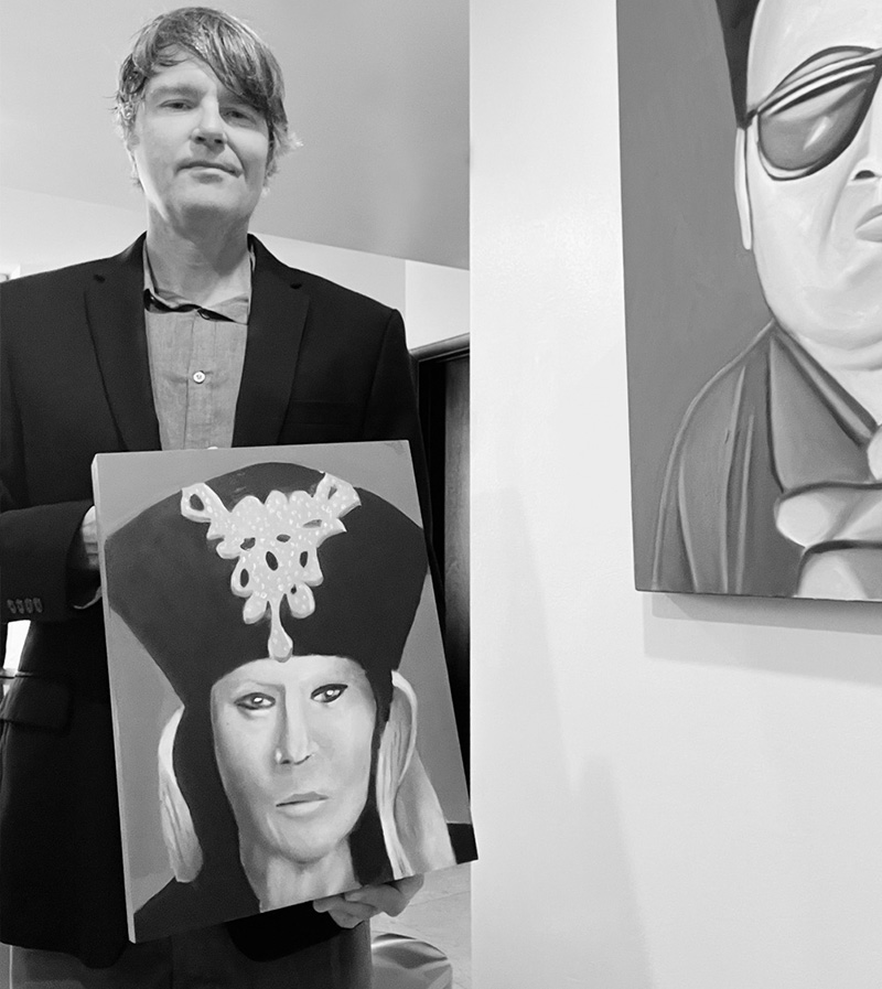 Man in a suit holding a painting of a woman in a tall headdress in an art gallery (black and white).