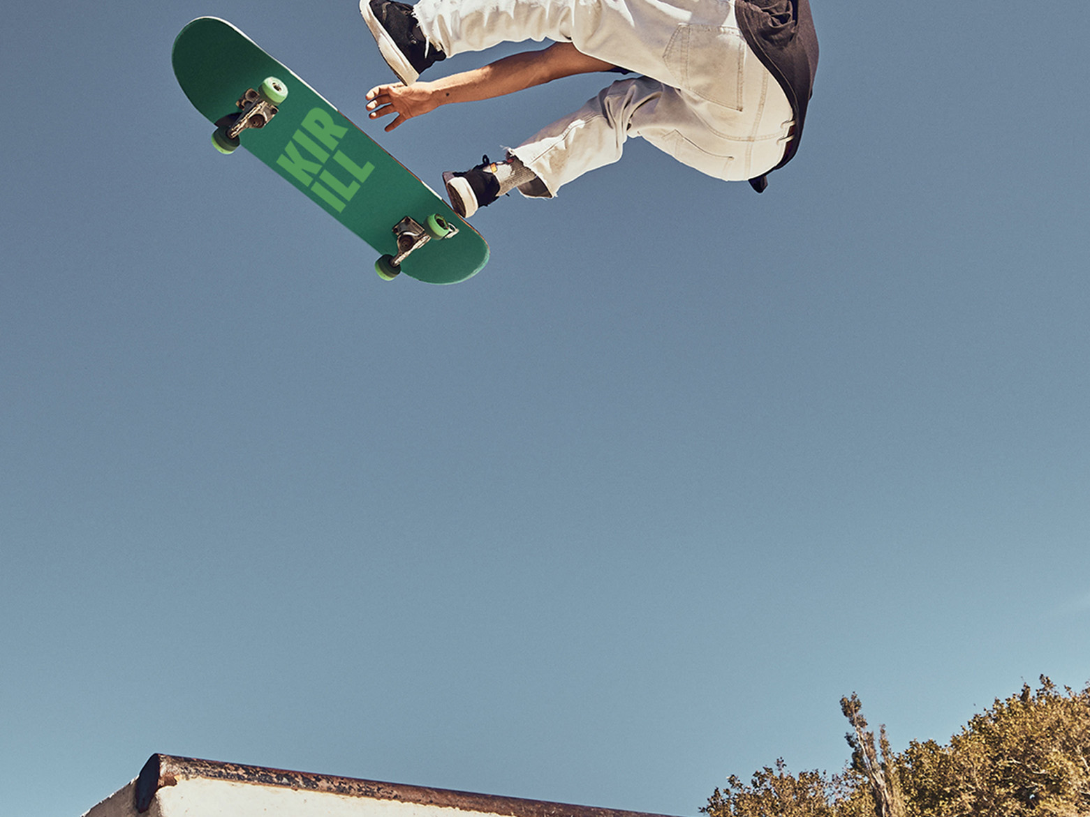 Skateboarder mid-air performing a trick with a green deck against a clear blue sky.”,