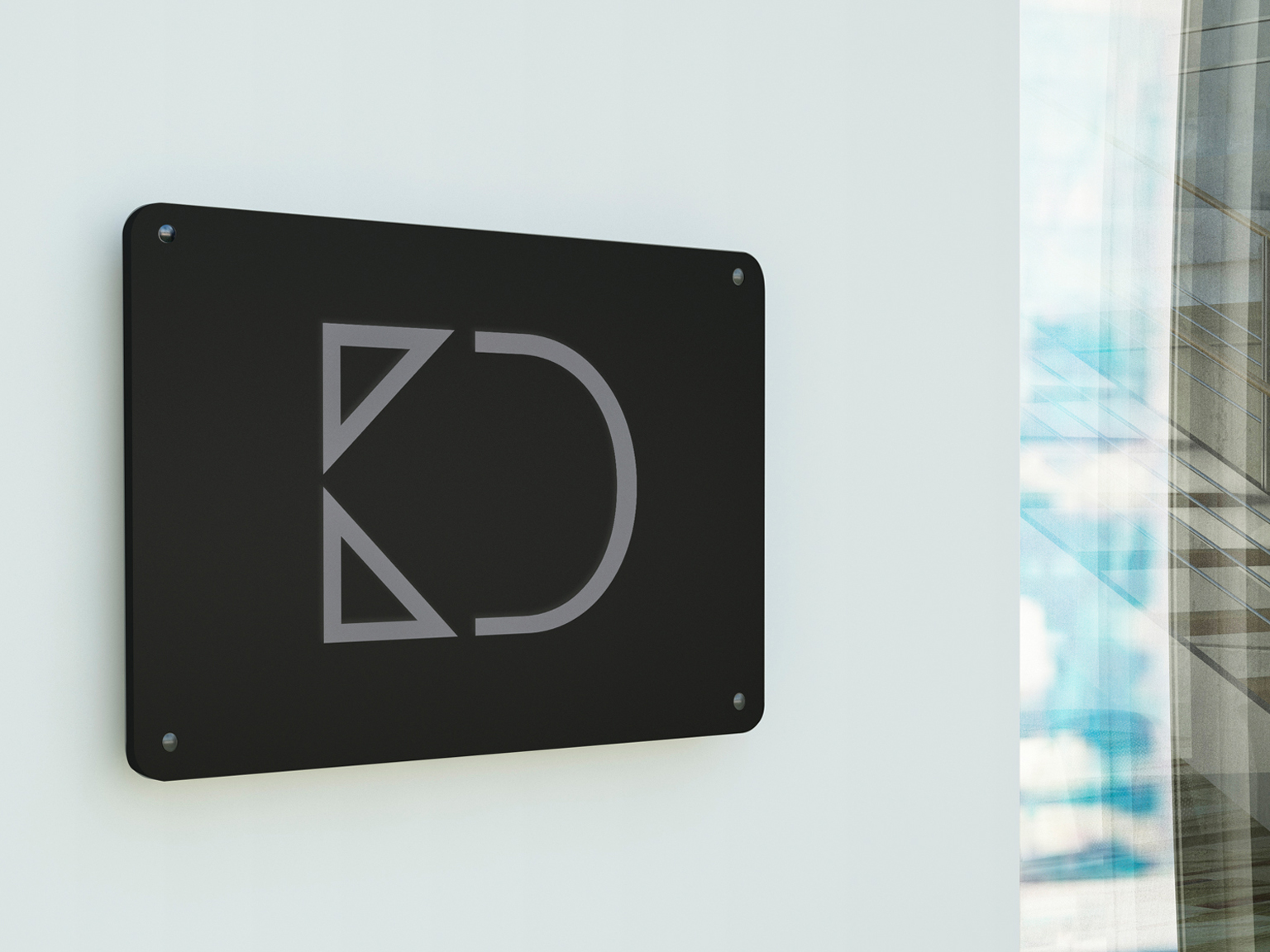 Black square sign with rounded corners displaying a gray geometric logo mounted on a light wall.